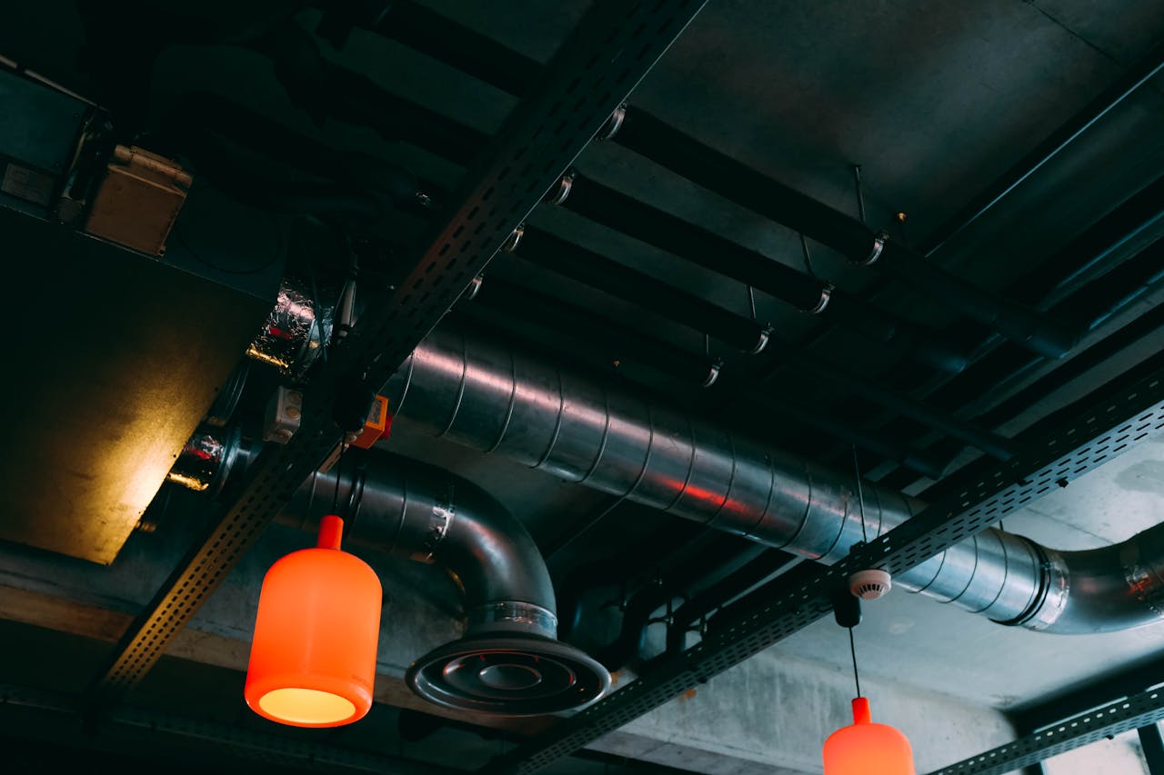 services-06 Low-angle view of a modern industrial ceiling featuring ducts and red lamps.